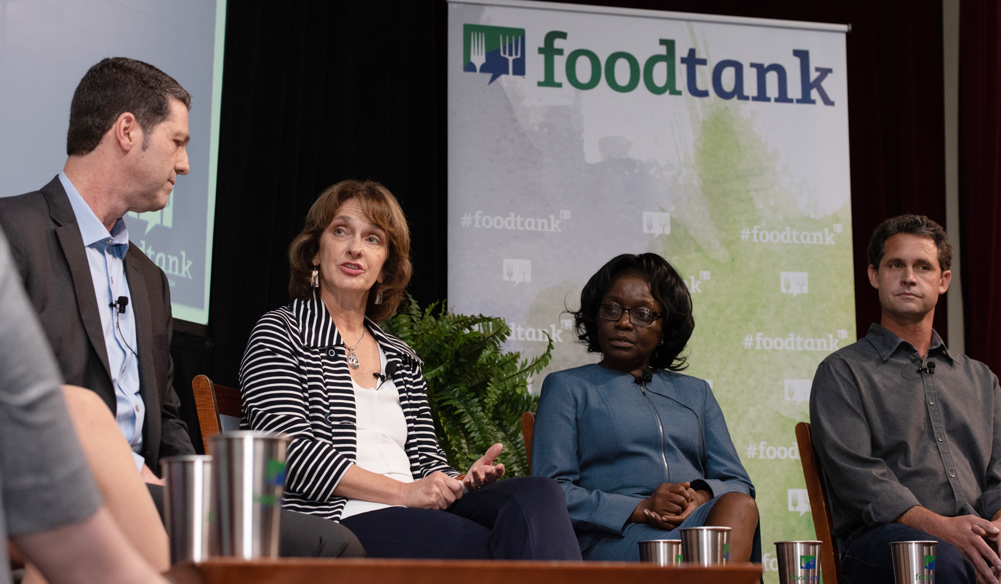 Beth Mitcham speaking on conference stage, next to Jane Ambuko, with two panelists listening, "foodtank" visible in background banner