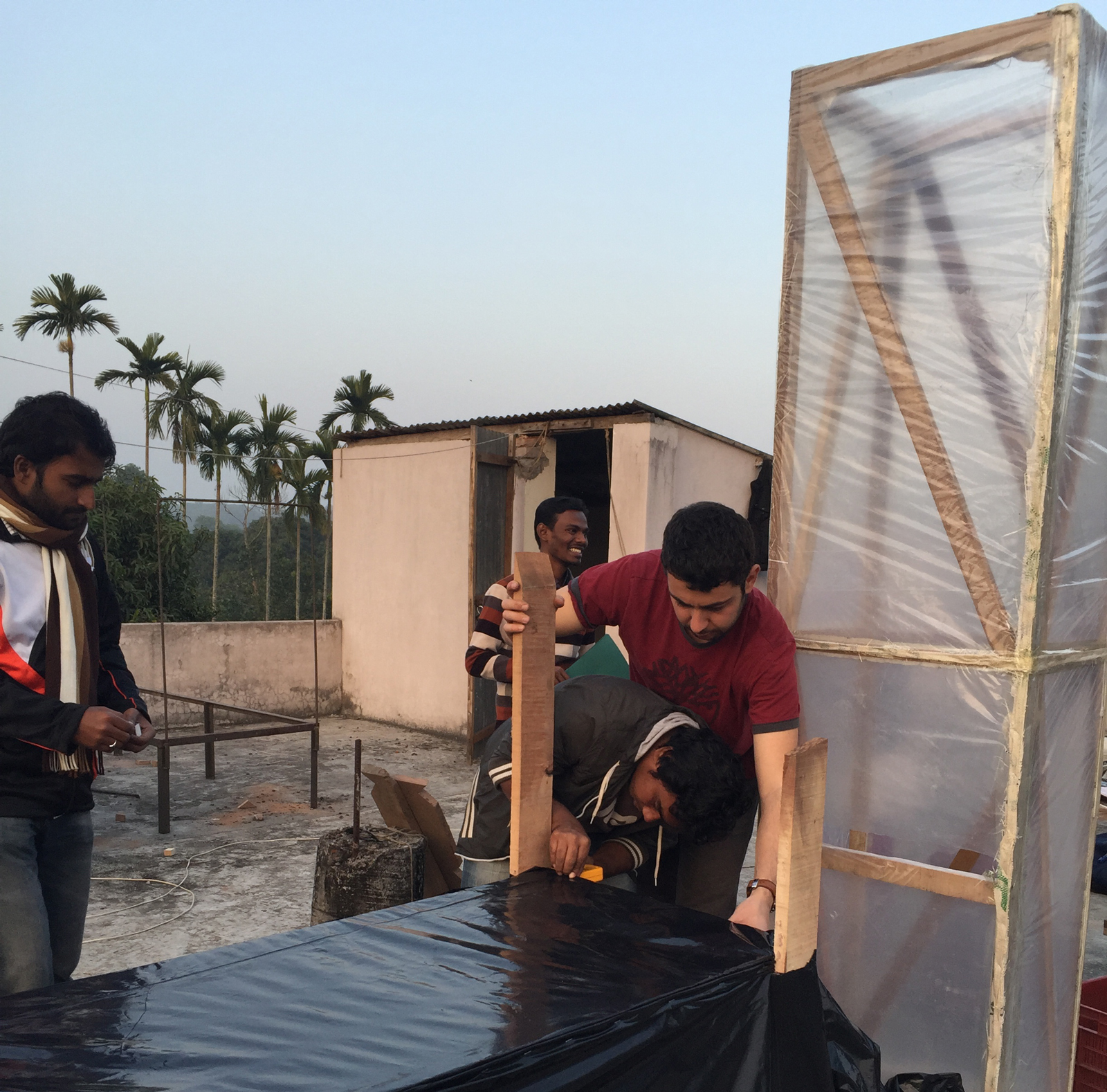 Two researchers connect a black table to a clear chimney to build a solar dryer
