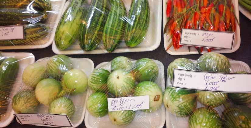 Fresh vegetables sit on Styrofoam trays covered in cling wrap with labels