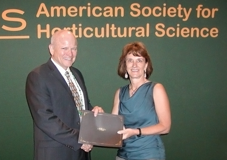 Two people stand holding a closed folder in front of banner reading "American Society for Horticultural Science "