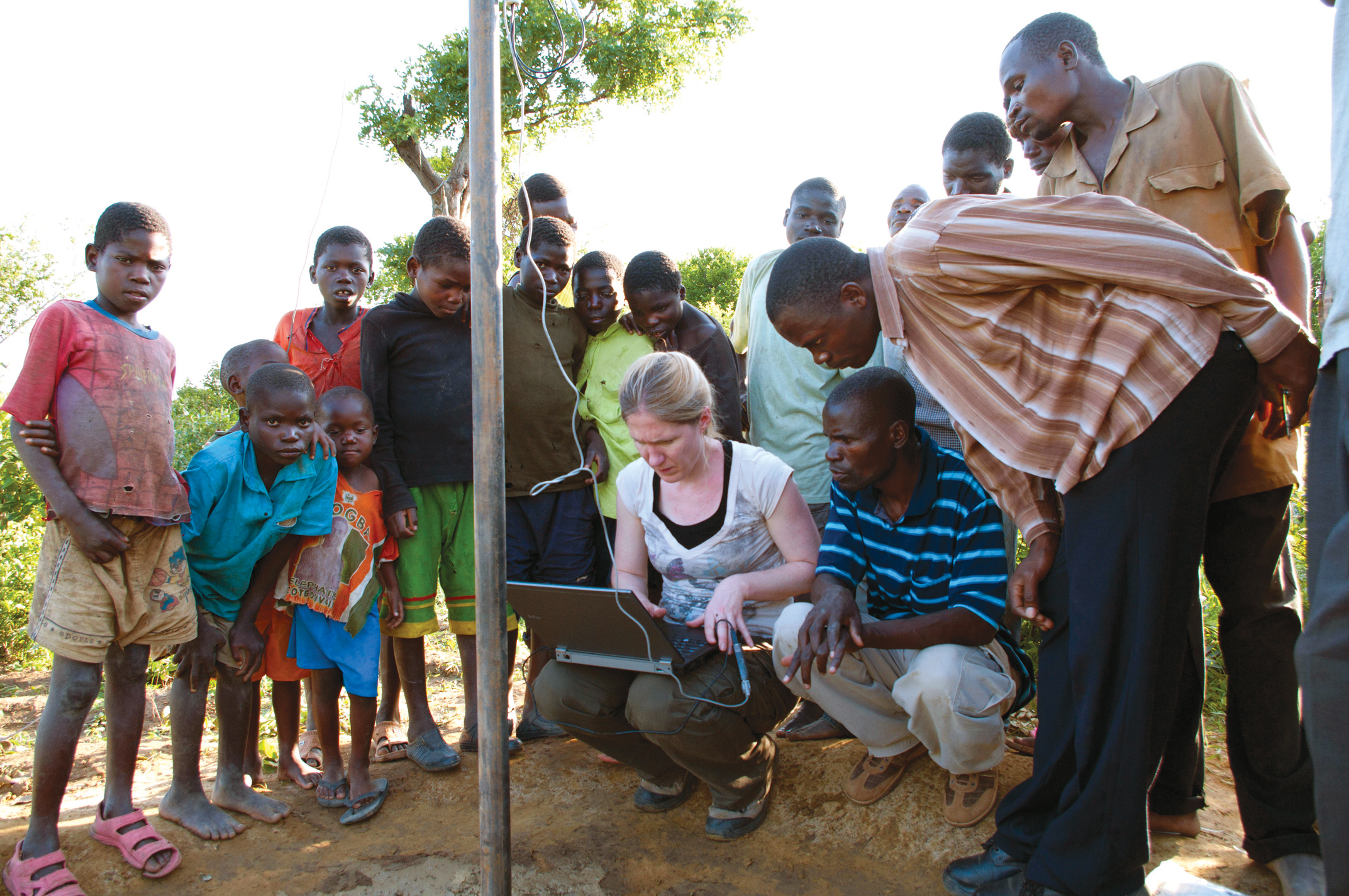Group gathers around Darcy Boellstorff as she plugs her computer into a GIS system near Mzimba.