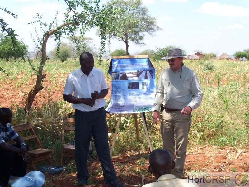 American and Kenyan men lead a farming extension class with poster, outside in Kenya