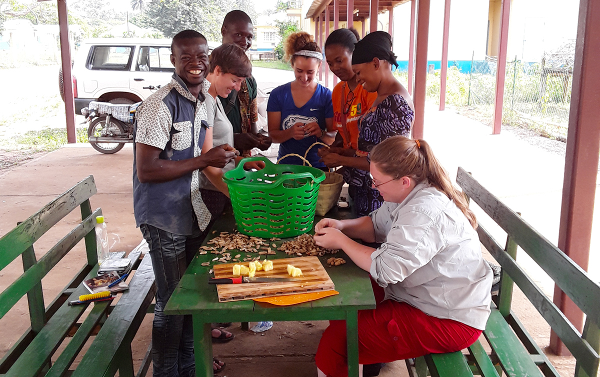 Horticulture Training and Services center staff, interns and AVENIRs de-shell peanuts under a shade structure. They are smiling. 