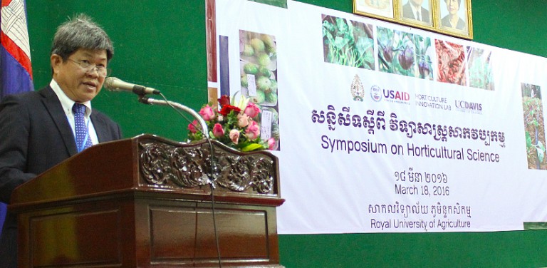 Bunthan speaks at podium, in front of a poster that reads "Symposium on Horticultural Science"