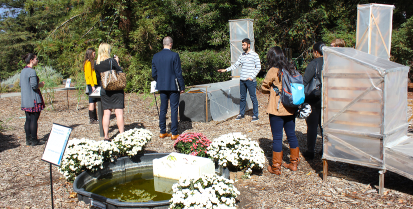 Group standing around a solar chimney dryer, Deltsidis is talking