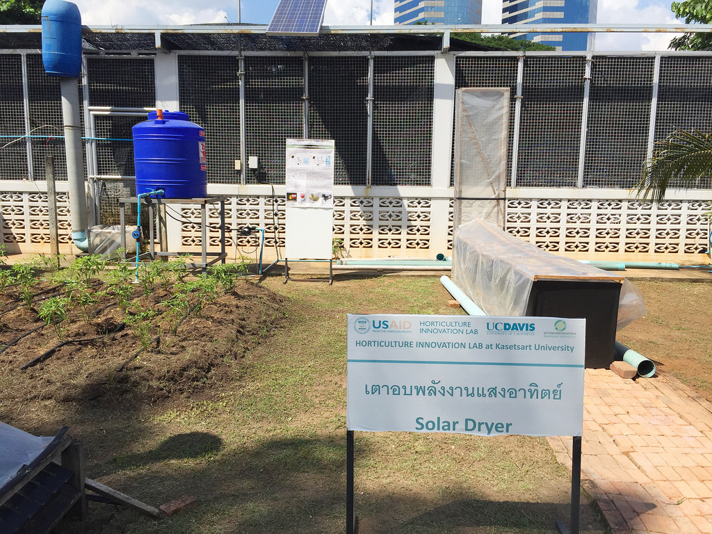 Sign with Thai words and "solar dryer" with chimney solar dryer and water tank in background