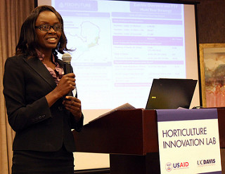 Woman stands at podium with microphone in front of a screen, podium reads "Horticulture Innovation Lab"