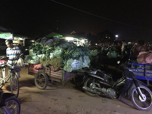 A wagon pulled by motorbike is piled high with bags of vegetables