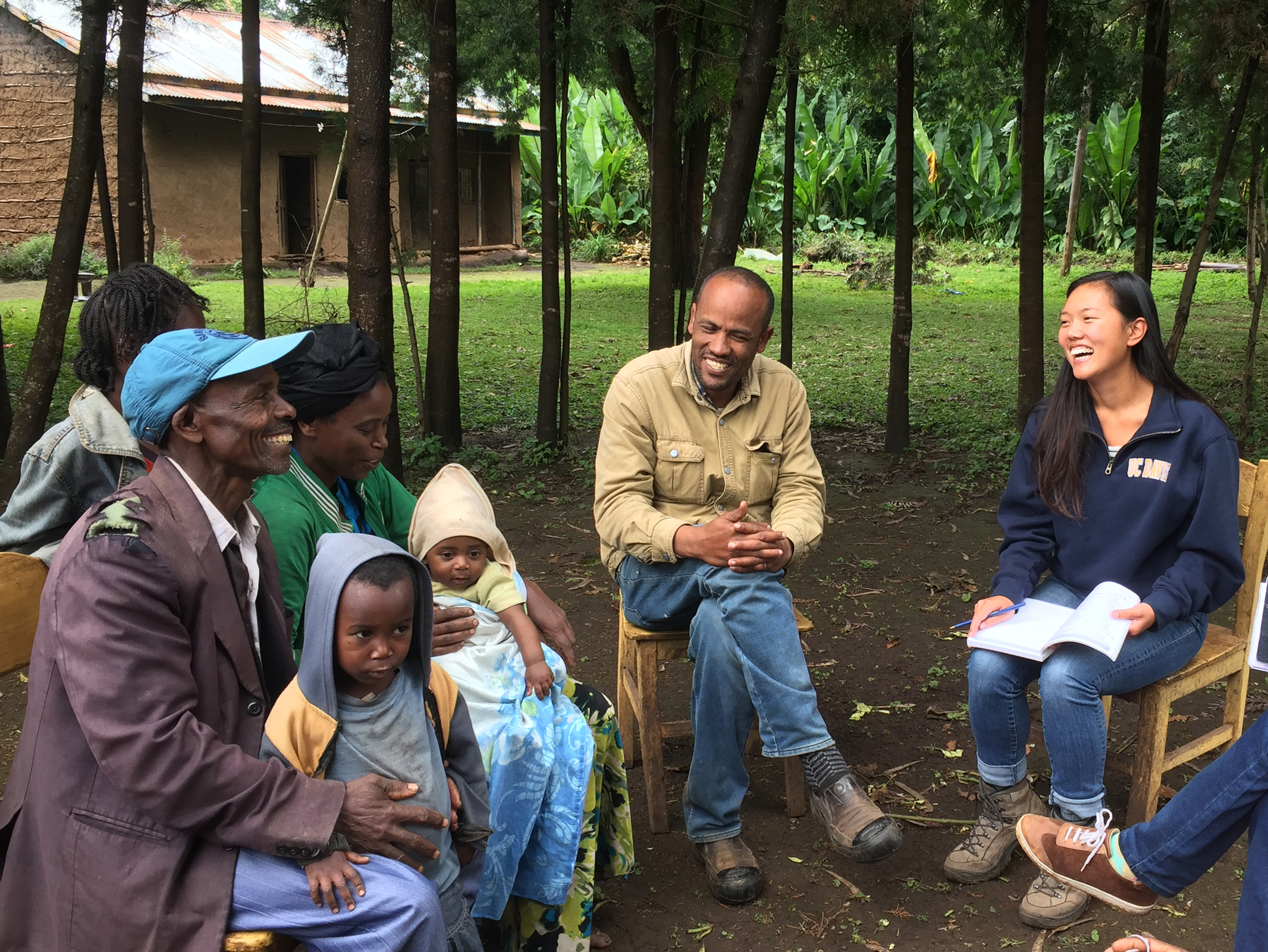 Seated outside in Ethiopia, group of farmers discusses sweet potato crop with local researchers and a UC Davis student