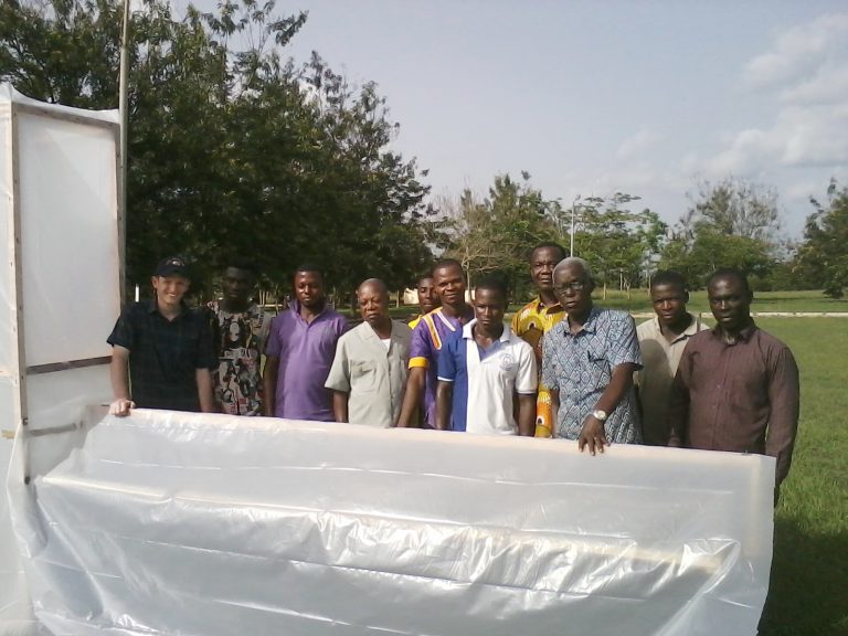 researchers with large solar dryer covered in clear plastic