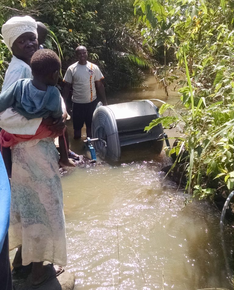 water-powered pump for irrigation in Uganda. Student in rivers shows of water wheel to woman farmer and child.