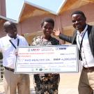 Niyidukunda Mugeni Euphrosine of Avo Healthy Oil Company grins and holds a giant check showing her award money from the competition, next to two other competitors.