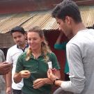 Grad student woman looking at paper test indicator offered by a Nepalese man, with group looking on at farm